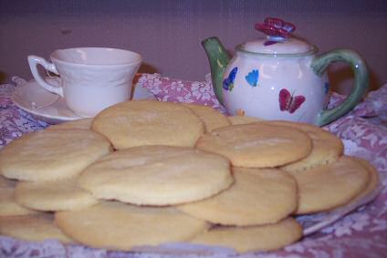 Net gebakken zandkoekjes op een bord met een kopje thee en theepot